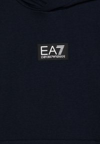 Felpa cappuccio blu navy con una texture liscia, caratterizzata da un'etichetta patch rettangolare nera che riporta la scritta "EA7 EMPORIO ARMANI" in caratteri bianchi.