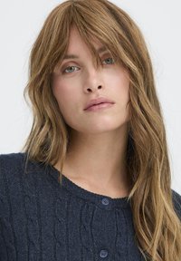 Námornícky pletený kardigán s okrúhlym golierom, s dvoma tmavými gombíkmi a štruktúrovaným vzorom. Mäkko, stredne ťažký pletený materiál.