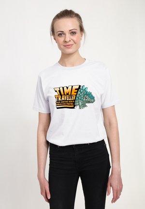 T-shirt bianca in cotone con un design grafico di un personaggio dinosauro e la scritta "TIME TRAVELLER" in grassetto nei colori nero e arancione.