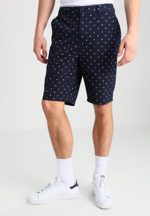 Granatowe spodenki w wzory z zapięciem na guzik, bocznymi kieszeniami i gładką tkaniną z małymi białymi motywami diamentów.