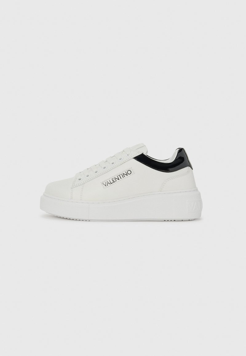 Hvite lerrets-sneakers med svarte lakk lærdetaljer; rund tå, tykk hvit såle, snøremekanisme og trykt "VALENTINO"-logo på siden.