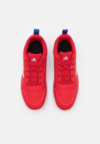 Zapatillas deportivas rojas con parte superior sintética lisa, interior negro, suela blanca y lengüeta azul en el talón. Presentan tres rayas blancas a lo largo del lateral.