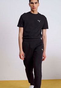 Sort kortærmet skjorte med et lille hvidt logo og matchende sorte joggingbukser med hvid tekst på benet, lavet af et behageligt stof.