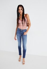 Camiseta de cuadros rojos y rosas, jeans azules y sandalias blancas de tiras. El conjunto tiene un ajuste relajado y un diseño casual.