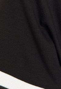 Tejido negro con textura acanalada, que presenta una tira blanca horizontal en la parte inferior. El material parece suave y elástico.