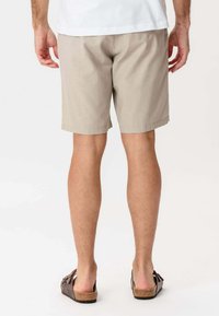 Beige shorts lavet af et let materiale, med et enkelt design, midt på låret og en lige skæring. Sammenstillet med brune sandaler.