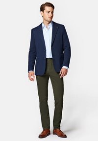 Granatowa marynarka o fakturze noszona na jasnoniebieskiej koszuli, zestawiona z oliwkowymi spodniami i brązowymi butami wizytowymi. Zapięta marynarka z dwoma kieszeniami.