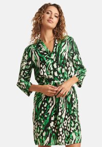 Grünes und schwarzes Kleid mit einem lebhaften Tiermuster, mit langen Ärmeln, einem Kragen und einem Bindegürtel in der Taille. Glattes, leichtes Material.