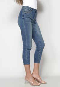 Jeans de mezclilla azules de cintura alta con una silueta ajustada, que presentan un dobladillo desgastado y adornos brillantes en los bolsillos frontales.