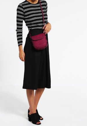 Nainen, jolla on päällään mustavalkoraitainen pitkähihainen paita, musta midihame, mustat avokkaat ja viininpunainen olkalaukku.