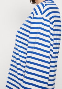 Långärmad randig skjorta i blått och vitt. Har en lös passform med breda ränder, mjuk tygtextur och rundad halsringning.