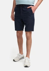 Pantaloni corti blu navy realizzati in un materiale morbido, con vita regolabile tramite coulisse, tasche laterali e taglio dritto, abbinati a sneakers bianche.