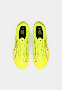 Lyse gule sportssko med et tekstureret design, med en rød accentstribe og et logo på ydersiden. Snørelukning og polstrede indersåler.