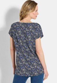 Haut à manches courtes bleu et gris à motif, avec un col rond et une coupe ample. Le tissu a une texture lisse et une silhouette fluide.