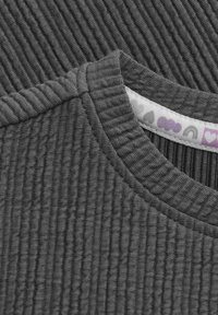 Szary prążkowany materiał z okrągłym dekoltem, prezentujący teksturowe wzory oraz kolorową metkę z małymi kształtami wzdłuż wewnętrznego szwu.