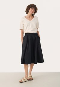 Beige V-hals t-shirt, zwarte geraffineerde rok met zakken, en beige sandalen met banden. Casual, ontspannen pasvorm; gladde stof en zachte textuur.