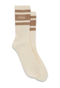 Pár ribbed smotanových ponožiek s hnedými horizontálnymi pruhmi a vyšitým logom "GUESS" blízko hornej manžety.