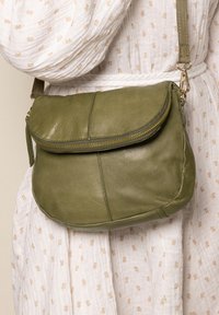 Olive green leather crossbody bag with a rounded shape, zip closure, and a flap. Features gold-tone hardware and a textured finish.