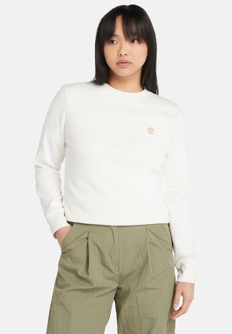 Vit crewneck sweatshirt i mjukt material, med en liten beige logotyp på bröstet. Matchad med ljusgröna plisserade byxor.