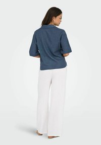 Camicetta blu scuro a maniche corte con finitura testurizzata, abbinata a pantaloni bianchi a gamba larga. Presenta un colletto e risvolti.