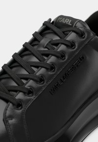 Svarta lädersneakers med texturerad yta, som har runda svarta öglor, svarta platta snören och det präglade "KARL LAGERFELD"-logotypen på sidan.