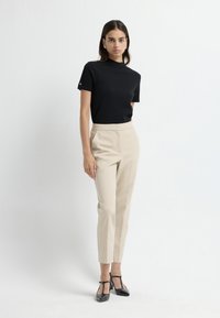 Zwarte top met korte mouwen, beige op maat gemaakte broek en zwarte schoenen met een lage hak. Gladde stof, aangesloten ontwerp en minimalistische accenten.