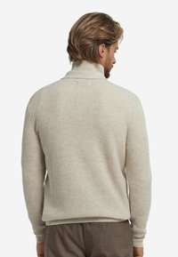 Beżowy sweter dziany z wysokim kołnierzem, teksturowanym wzorem, dopasowanymi rękawami i ściągaczem, widoczny od tyłu.