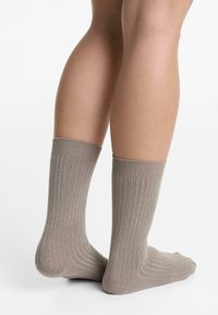 Legs wearing mid-calf ribbed beige socks, standing against a plain white background.