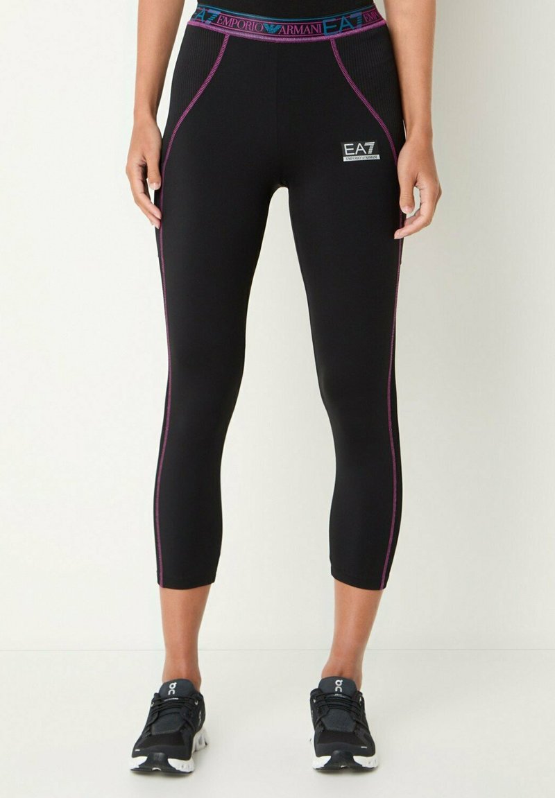 Leggings capri neri realizzati in tessuto elasticizzato, con una linea decorativa viola, cintura con marchio e logo EA7 sul lato.