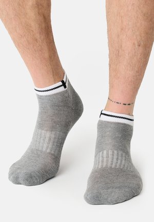 Nogi w niskich szarych skarpetkach z białymi i czarnymi paskami na mankietach, ukazujące tatuaż w formie przerywanej linii na prawym kostce.