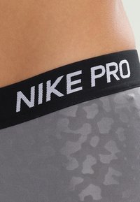 Pantaloni sportivi grigi con una cintura elastica nera contrassegnata con la scritta "NIKE PRO" in lettere bianche; il tessuto presenta una texture a motivi sottile.