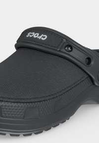 Sabot Crocs noir texturé avec bride de talon réglable, logo Crocs blanc et trous de ventilation sur le côté.