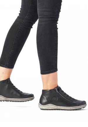 Bottes montantes en cuir noir avec une fermeture éclair sur le côté et une semelle texturée. Agrémentées d'un logo circulaire et de surpiqûres le long du bord.