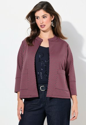 Leichte rot-blau karierte Jacke mit Dreiviertelärmeln, rundem Halsausschnitt und Seitentaschen. Über einem dunklen Oberteil getragen.