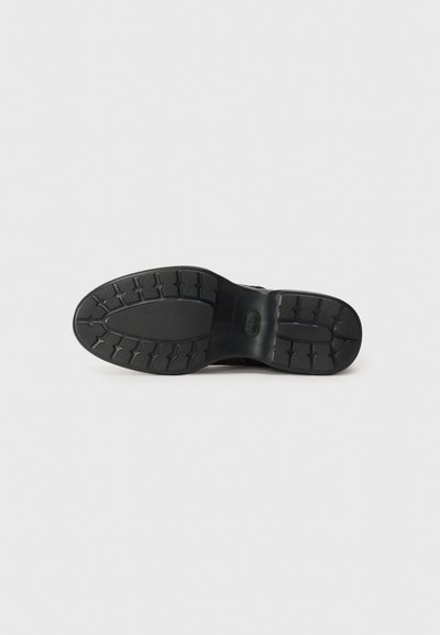 Semelle de chaussure en caoutchouc noir avec un motif texturé, présentant une zone centrale lisse et un logo en relief. Conception légère adaptée à un usage décontracté.