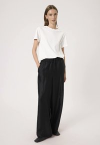 Weißes Baumwoll-T-Shirt kombiniert mit schwarzen, weit geschnittenen, zerknitterten Stoffhosen. Die Hosen haben einen elastischen Bund und Seitentaschen.