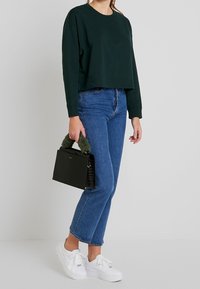 Zielona krótka bluza, niebieskie dżinsy z wysokim stanem, białe tenisówki oraz czarna torebka o teksturowanej powierzchni z zielonym futrzanym uchwytem.