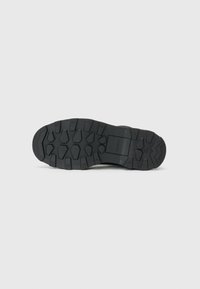 Semelle de chaussure noire avec des rainures profondes, présentant un motif géométrique pour l'adhérence. Fabriquée en caoutchouc, texturée pour la durabilité.