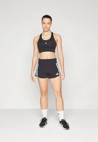 Top desportivo e calções pretos com o logo da Adidas, combinados com sapatilhas pretas e meias brancas até ao meio da canela, sobre um fundo neutro.