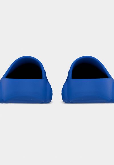 Ζευγάρι μπλε λαστιχένιες παντόφλες χωρίς κορδόνια με λουράκια στη φτέρνα, σε θέα από μπροστά πάνω σε απλό ανοιχτό φόντο.