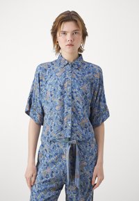 Sininen kukallinen lyhythihainen paita, jossa on kaulus. Paidassa on paisley-kuvioita, napit edessä ja rento leikkaus.