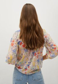 Blumenbluse aus leichtem Stoff, mit hellen Mustern aus roten, lila und gelben Blumen, langen Puffärmeln und einem abgerundeten Saum.