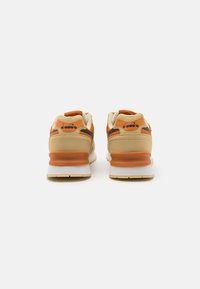 Beige and orange athletic shoes with a cushioned sole, textured panels, and a logo on the back. Durable materials and supportive design.