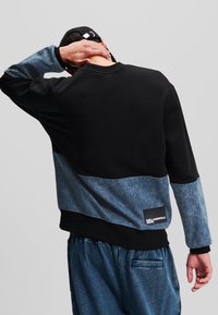 Mustat hupparit, joissa on denimsininen alaosa. Liipeä pinta, pitkät hihat ja merkillä "Karl Lagerfeld Jeans" varustettu tuote.