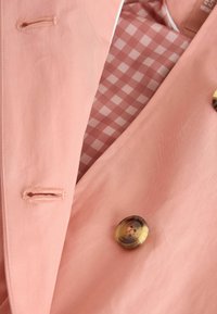Light pink jacket featuring a smooth texture, large tortoiseshell button, and a gingham patterned lining in shades of pink and white.
