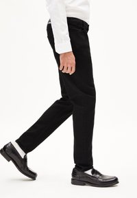 Zwarte denim broek met een slim fit, met een gemiddelde taillehoogte en traditionele zakken. Gepaard met gepolijste zwarte loafers en witte sokken.