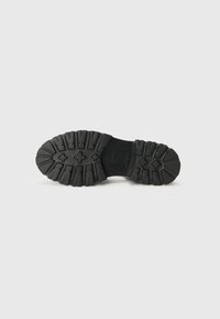 Suola di scarpa in gomma nera caratterizzata da un design del battistrada robusto con scanalature profonde e motivi in rilievo per una maggiore trazione e durata.