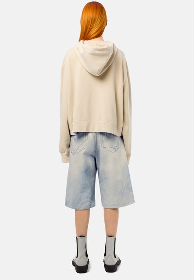 Hoodie beige court avec une capuche à cordon de serrage, associé à un short en denim bleu clair. Les chaussures présentent des accents gris et une finition texturée.