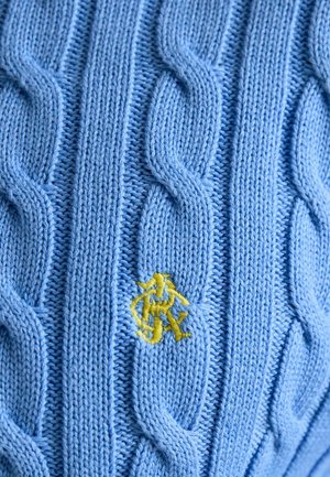 Jasnoniebieska dzianinowa tkanina z pionowymi wzorami warkoczy oraz małym żółtym wyszywanym monogramem umieszczonym blisko środka.