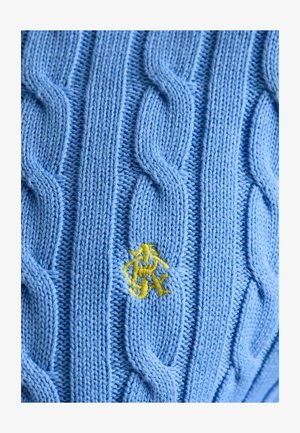 Jasnoniebieska dzianinowa tkanina z pionowymi wzorami warkoczy oraz małym żółtym wyszywanym monogramem umieszczonym blisko środka.